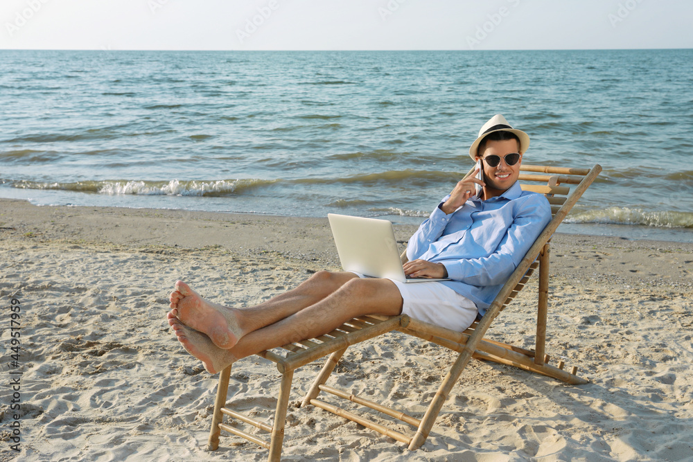 Happy man with laptop talking by mobile phone on beach. Business trip