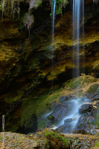 A small waterfall in the shade  on the slope of a rocky cliff in the forest. Shot with a long exposure.