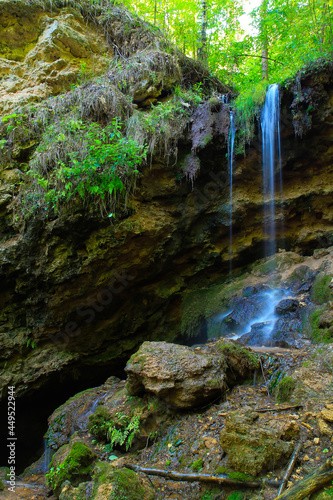 A small waterfall in the shade  on the slope of a rocky cliff in the forest. Shot with a long exposure.