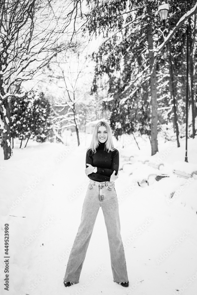 Black-white photo of a  woman in a black sweater and jeans posing on a background of winter street