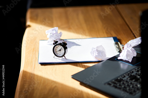 Modern workplace, wooden office desk in hardlight, sunligt with clock, sheet of paper