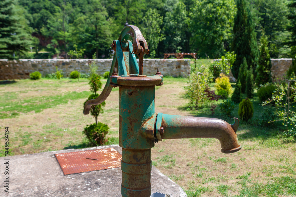 An old fashioned hand operated green rusty water pump, nature background