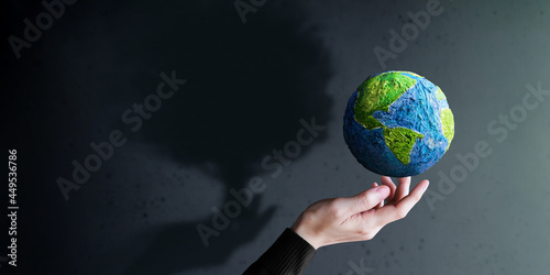 Fototapeta Naklejka Na Ścianę i Meble -  World Earth Day, ESG Concept. Green Energy, Renewable and Sustainable Resources. Environmental and Ecology Care. Hand Gesture Levitating a Green Handmade Globe. Big Tree Shadow shading on the Wall