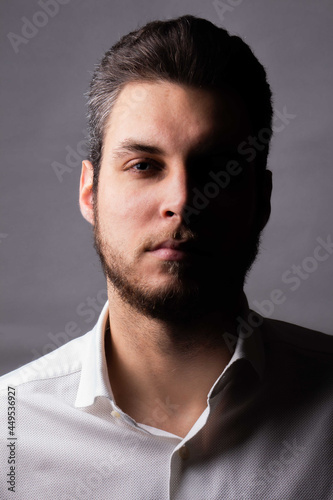Studio portrait of a caucasian man wearing a shirt with confident and secure expression, half of the face in shadow, person isolated on white background - confident millennial businessman concept