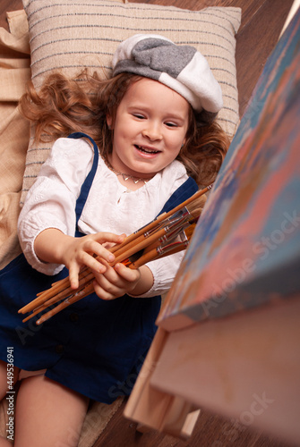 A talented little girl artist working on a modern abstract oil painting, gesturing with a brush with wide strokes. Artistic palette. Contemporary art paint on canvas, creative, contemporary and succes