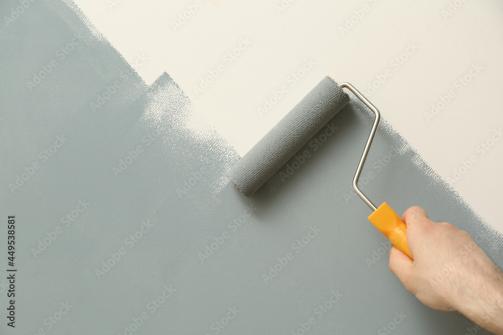 Man applying grey paint with roller brush on white wall, closeup - obrazy, fototapety, plakaty 
