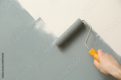 Man applying grey paint with roller brush on white wall, closeup photo