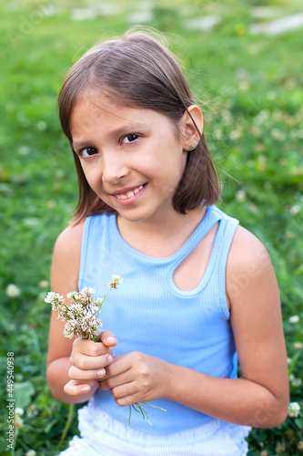 A cute little girl in a meadow on a summer day smiles and looks at the camera, holding a bouquet of summer flowers in her hands.