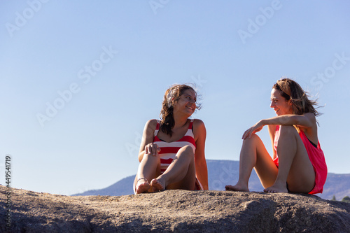 Two young women talking and laughing on a rock on a sunny day. Friends. Copy space. Selective focus.