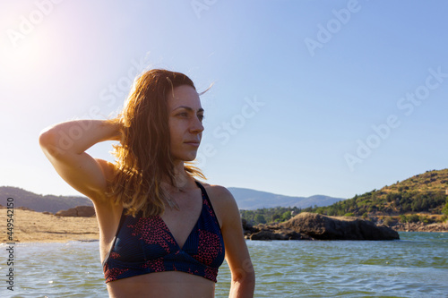 Young woman in bikini holding her hair in a lake. Summer. Copy space. Selective focus.