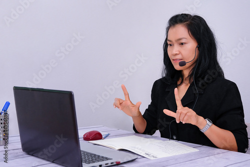Asian young businesswoman student-teacher tutor wear wireless headset video conference show sign language computer talk by webcam learn to teach online chat, distance webinar online teaching concept