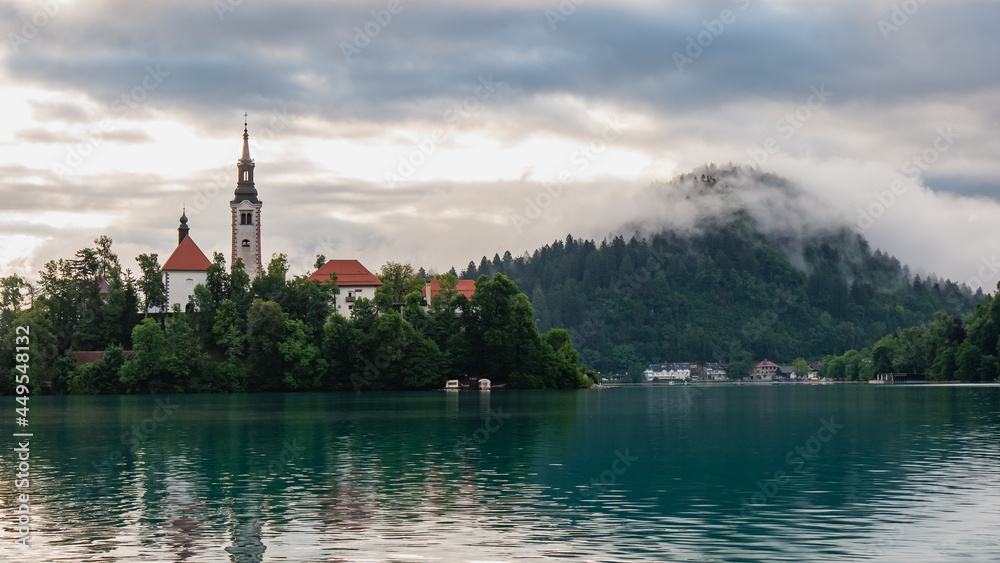 View of beautiful Lake Bled (Blejsko Jezero) with the Pilgrimage Church of the Assumption of Maria on a small island and Bled Castle and Julian Alps at backgroud at summer time.
