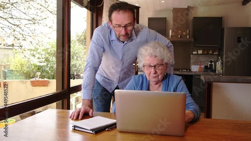 mature man helping elderly senior woman at home with paperwork and computer internet lesson
