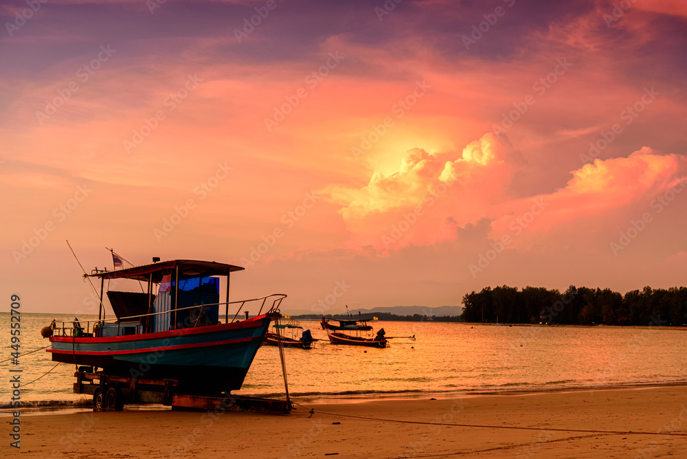 Silhouette of fishing boat on sea beach with sunset background.