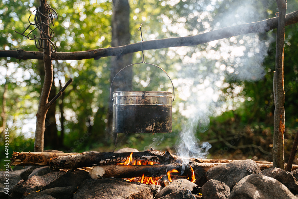 A tourist soot-covered bowler hat hangs over a smoking campfire at a forest camp in summer. Camping cooking. A tourist soot-covered bowler hat hangs over a smoking campfire at a forest camp in summer. Camping cooking.