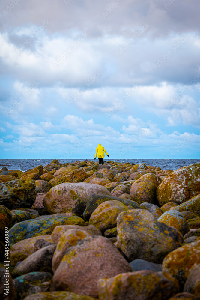 Obraz premium A woman in a yellow winter jacket walking on a rocky Ainazi pier dividing Latvia and Estonia by the Baltic Sea