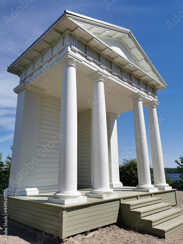 The Temple of Neptune with white columns in the rocky natural park of Monrepos in the city of Vyborg against the background of a blue sky with clouds.