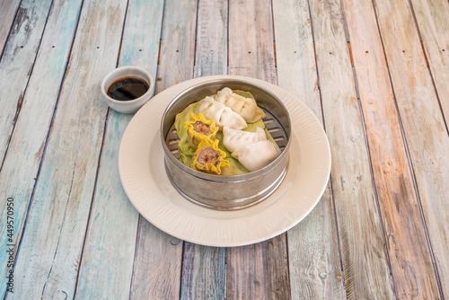 Dim sum and assorted gyozas steamed in a stainless steel bowl with soy sauce for dipping cooked by a Chinese chef photo