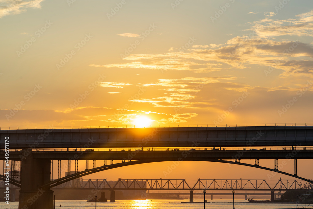 The bridge over the river against the backdrop of a bright orange sunset.