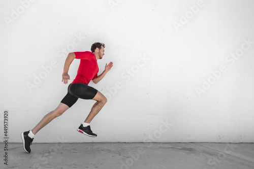 Fitness running man runner profile on wall white background. Male sports athlete sprinting with hiit high intensity interval training workout wearing compression sportswear clothes.