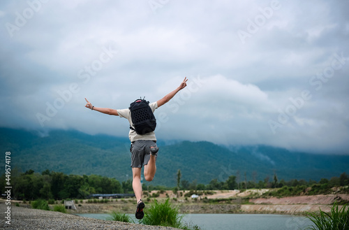 Back view point of young man backpacker jumping over the ground and raising his arm with victory sign , freedom , inspiration and motivation concept