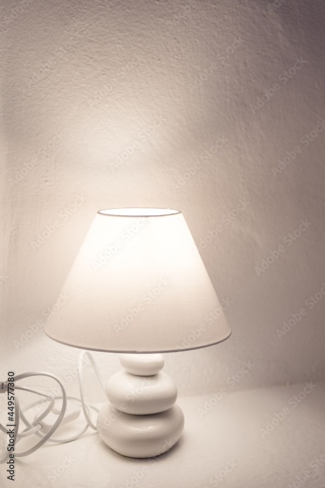 Close-up of burning lamp on nightstand. White stone wall. Close-up of burning lamp on nightstand. White stone wall.