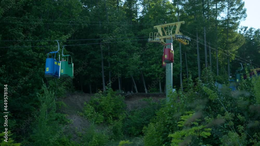 Many funiculars blue red and green ride down and up against the background of a green deciduous forest Many funiculars blue red and green ride down and up against the background of a green deciduous forest