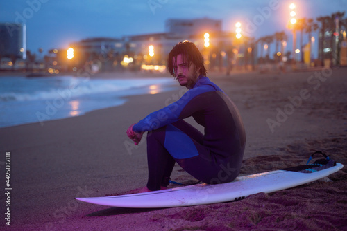 Εκτύπωση καμβά Night portrait of surfer in neoprene suit sitting on his surf board and looking