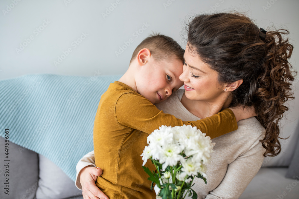 Tender son kisses the happy mother and gives her a bouquet of flowers, congratulating her on mother's day during holiday celebration at home. Family holidays and celebration concept Tender son kisses the happy mother and gives her a bouquet of flowers, congratulating her on mother's day during holiday celebration at home. Family holidays and celebration concept