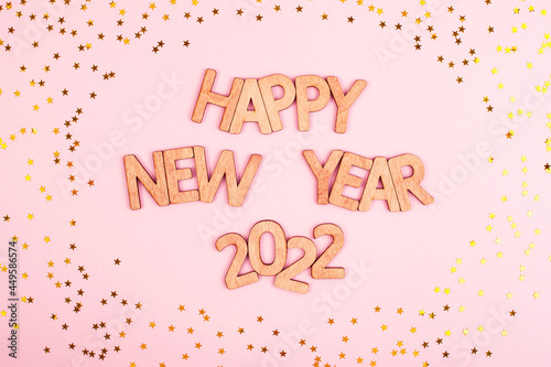 New Year's inscription happy new year 2022 in wooden letters on a pink background with stars. A New Year's card.