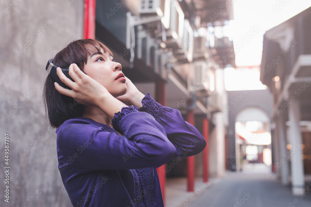 Happy young asian woman listening to music with headphones on the street.
