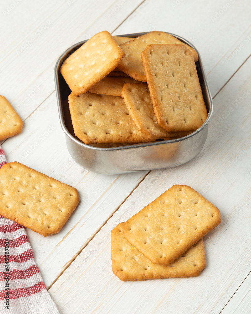Cracker cookies in a stainless steel bowl with tablecloth on white wooden table background. Cracker cookies in a stainless steel bowl with tablecloth on white wooden table background.