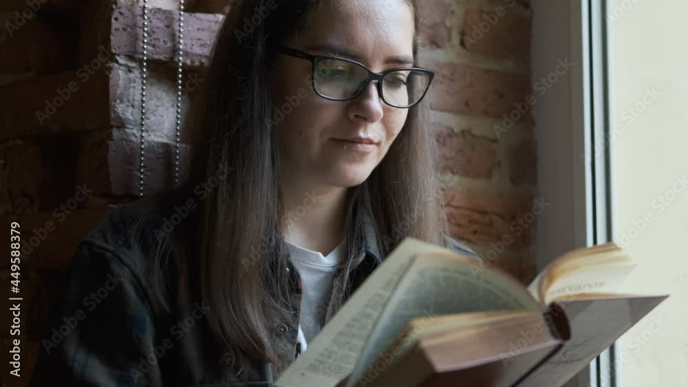 portrait of a stylish woman with glasses reading a book by the window portrait of a stylish woman with glasses reading a book by the window