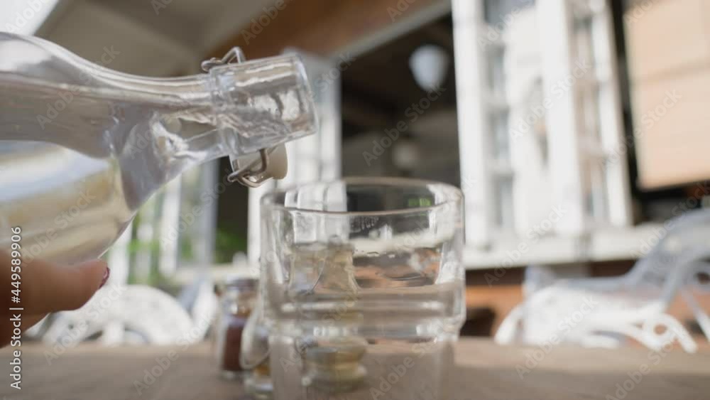 The waiter pours water from a bottle into a clear glass glass standing on the table. The summer terrace of the restaurant on a sunny day, without people. An empty restaurant with one customer. Slow. The waiter pours water from a bottle into a clear glass glass standing on the table. The summer terrace of the restaurant on a sunny day, without people. An empty restaurant with one customer. Slow.