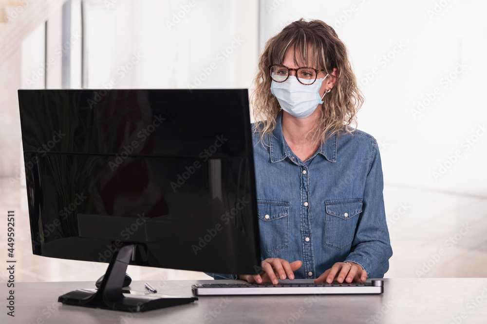 Adult woman wearing protective face mask in office using computer Adult woman wearing protective face mask in office using computer