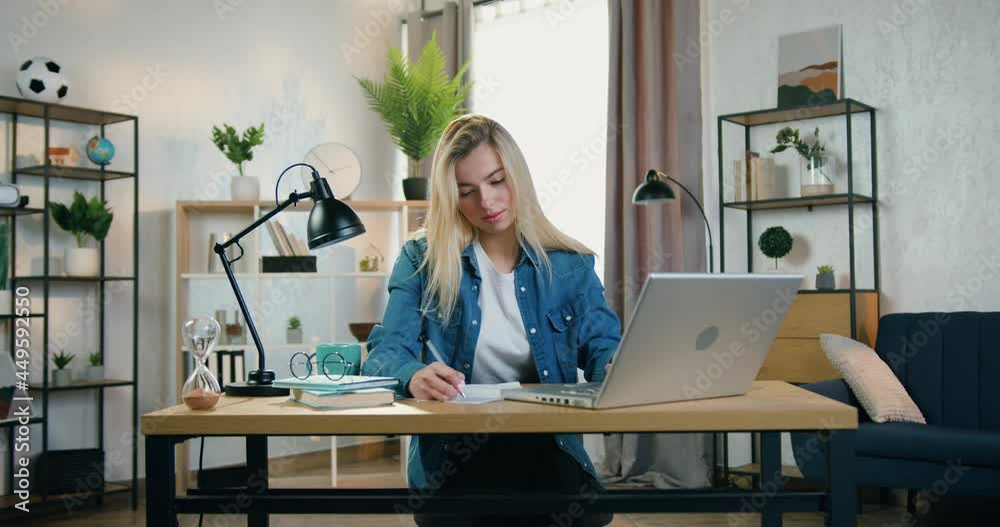 Close up of likable confident experienced blond female worker which sitting in home office and remotely working over start up project and doing notes into papers