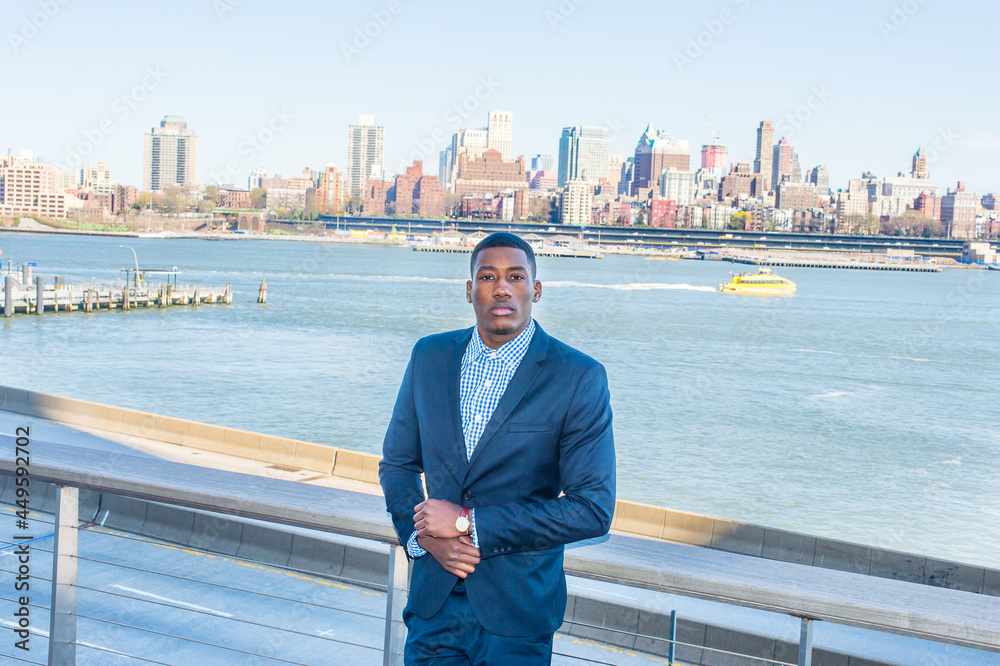 A young black businessman is standing by the river, confidently looking at you. Background is an old big city scene.. A young black businessman is standing by the river, confidently looking at you. Background is an old big city scene..