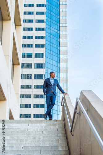 A young handsome black businessman is standing outside of a business building, confidently looking forward..
