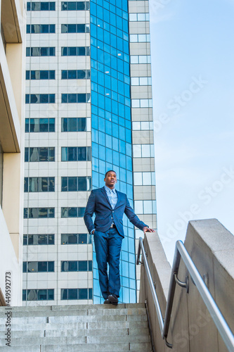 A young handsome black businessman is standing outside of a business building, confidently looking forward.. © Alexander Image