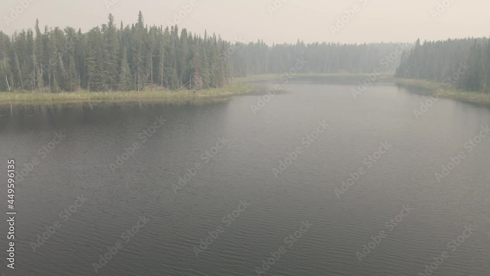 Drone flying slowly forward and rising over a small lake that is covered in thick wildfire smoke.
Drone flying slowly forward and rising over a small lake that is covered in thick wildfire smoke.