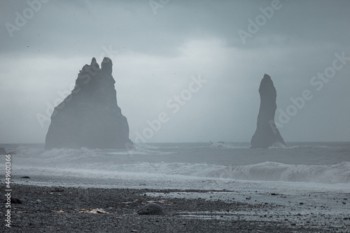 Reynisfjara beach in Iceland with big basalt pillars climbing from water and rocky beach. Cold windi place at the beach with big waves. photo