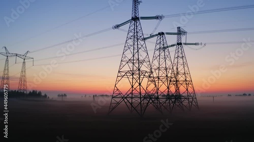 Aerial view high voltage steel power pylons in field covered with fog countryside. Misty morning, dawn. Drone flight low over power transmission lines. Electric tower line, sunrise sunset