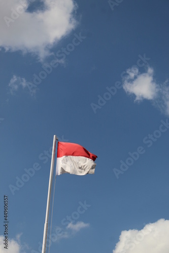 The red and white flag of Indonesia is flying in the blue and cloudy sky