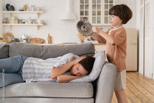 Bilde på lerret Tired overwhelmed mother cover ears with hands lying on sofa at home with misbeh