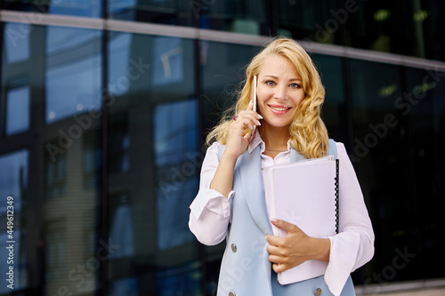 Happy woman in business suit talks by cellphone outdoors.