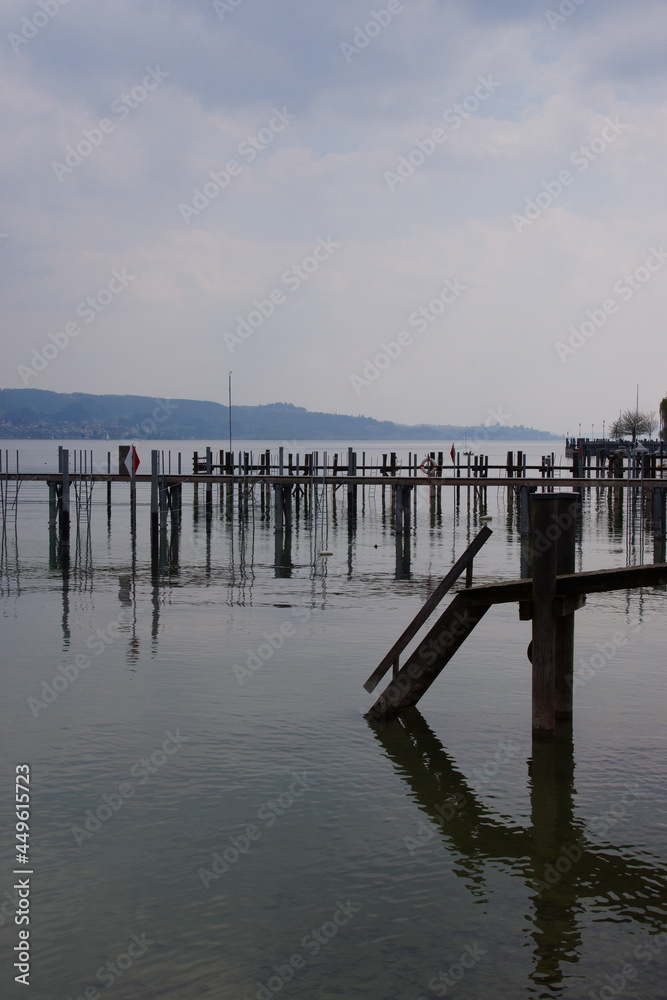Bootsanlegestelle und Pier am Bodensee (Deutschland, Europa) bei bedecktem Himmel; die Pfahlkonstruktionen bilden ein interessantes geometrisches Muster; die Stimmung ist ruhig und sehr entspannt