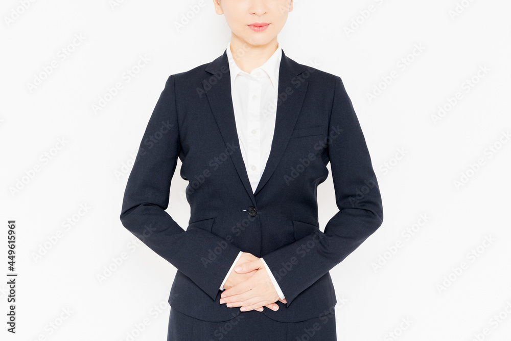 白背景の前に立って、お腹に手を当てるスーツを着たビジネスウーマン