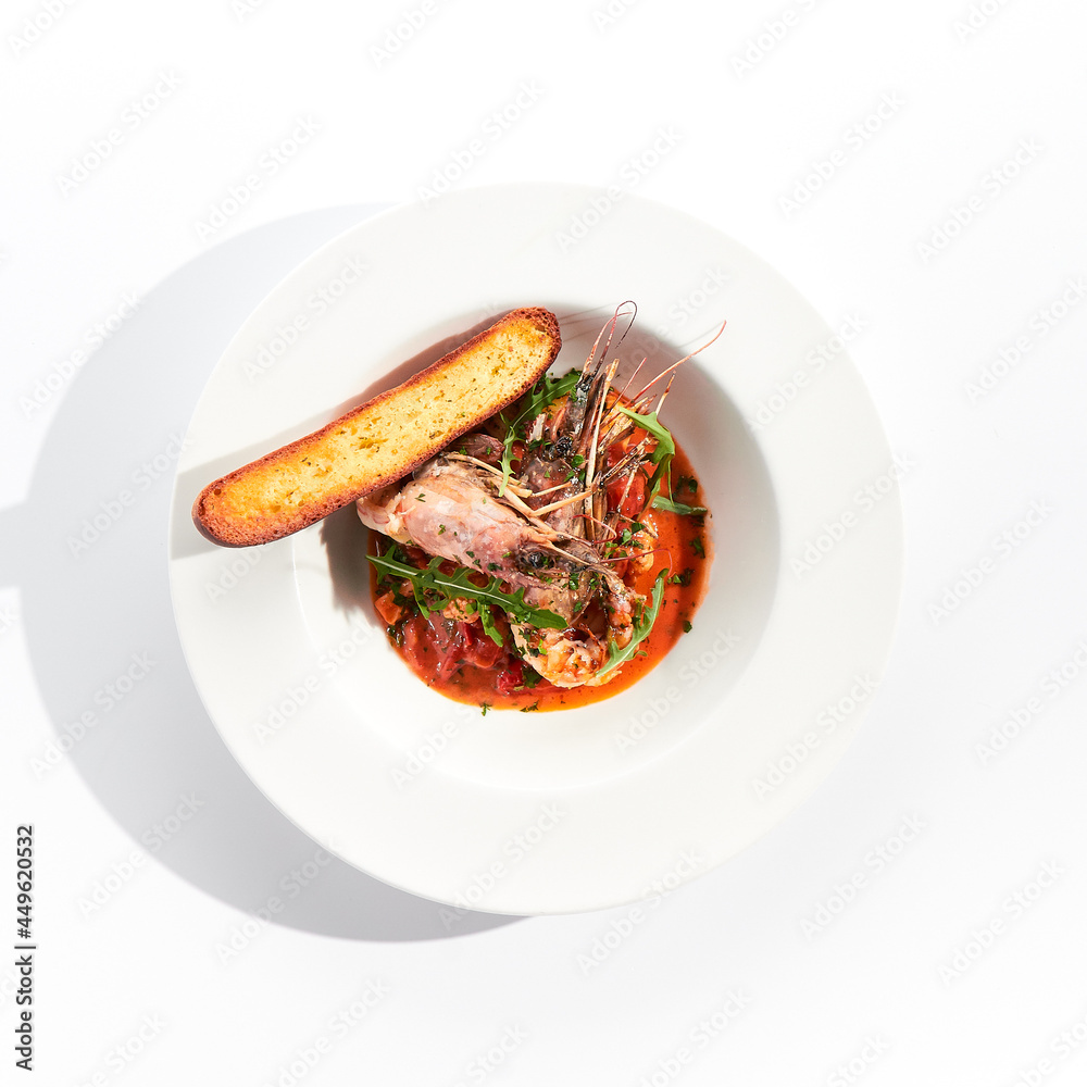 Seafood with tomato sauce on white restaurant plate. Shrimp seafood and tomato stew garnished with fried bread. Isolated on white background. Seafood with tomato sauce on white restaurant plate. Shrimp seafood and tomato stew garnished with fried bread. Isolated on white background.