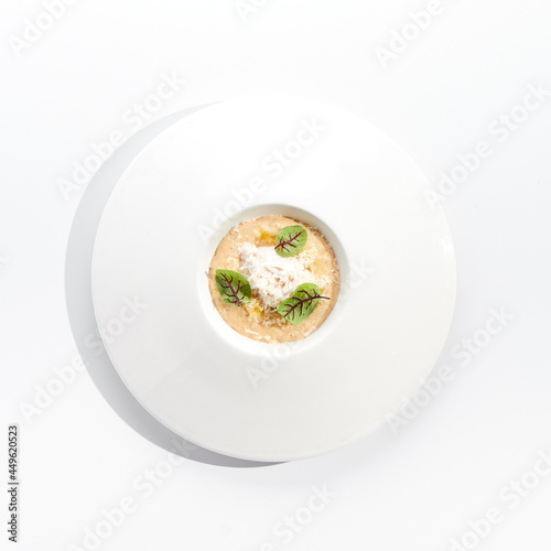 Risotto with crab meat in white restaurant plate. Garnished with Parmesan cheese and green leaves. Delicious crab meat risotto with white sauce isolated on white background. Rice with seafood.
