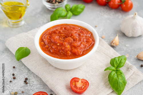 Traditional Italian marinara sauce in a bowl on a concrete background with spices and ingredients. Copy space.